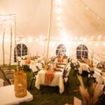 A wedding venue tent with dinner equipment on tables and string lights